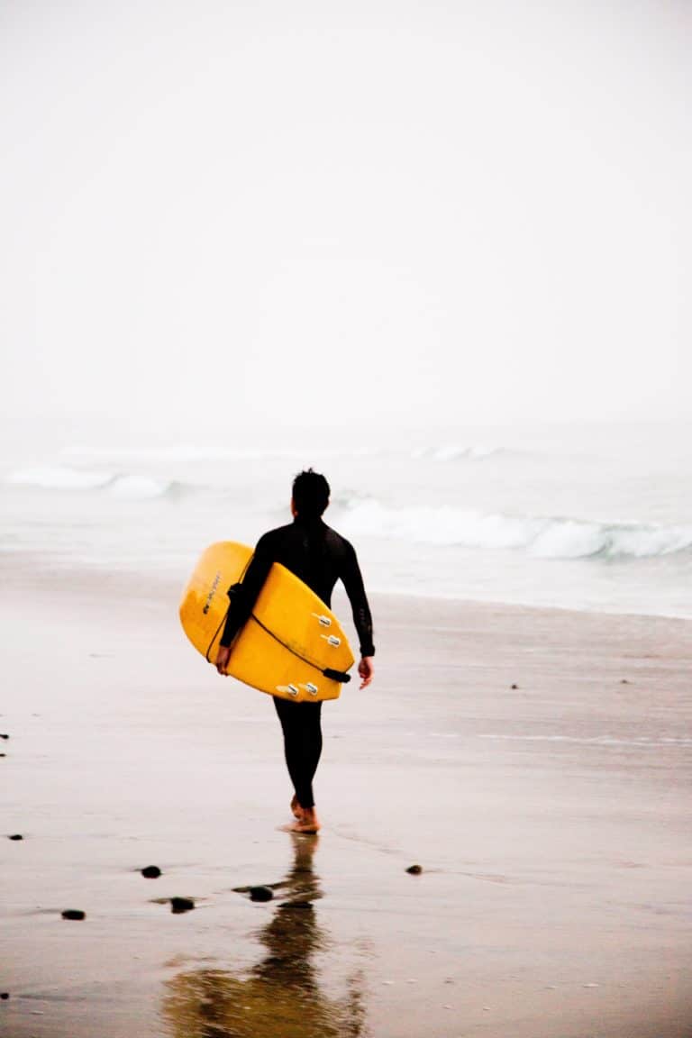 Surfeur marchant sur la plage avec une planche jaune.